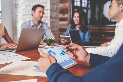 real estate colleagues discuss the inflation rate around a conference table while viewing laptops and tablets